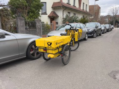 Almanya - 18 Şubat 2023: Meşgul bir Alman caddesi, arabalar, elektrikli bisiklet ve sarı bir Deutsche Post posta paketi bisikleti gibi çeşitli araçlarla görüldü