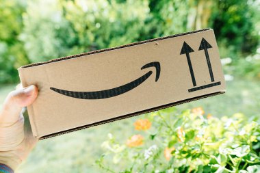 Hamburg, Almanya - 24 Temmuz 2023: POV erkek, bahçe yeşili arka planı olan yeni Amazon Prime karton paketini tutuyor