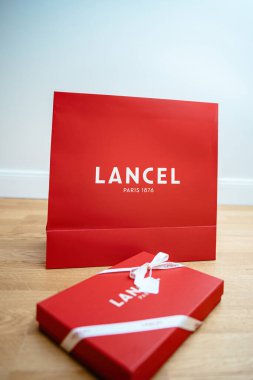 Paris, Fransa - 25 Ağustos 2023: Lancel Paris 'in ön manzarası ahşap zeminde zarif logolar ve ipek kurdelelerle damgalanmış kırmızı hediye kutusu. Lüks ve sofistike bir sembol. Sunumlar için mükemmel