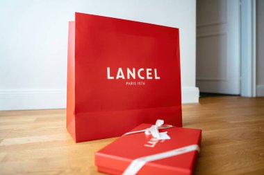 Paris, Fransa - 25 Ağustos 2023: Lancel Paris 'in yan görünüşü, ahşap zemininde zarif logolar ve ipek kurdelelerle damgalanmış kırmızı hediye kutusu. Lüks ve sofistike bir sembol. Sunumlar için mükemmel