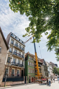 Strasbourg, Fransa - 7 Temmuz 2023: Canlı sarı bir vinç, kendini adamış işçilerin zengin bölgeleri koruyarak büyüleyici bir Alsas evini restore ettikleri bir yaya caddesinin ortasında duruyor.