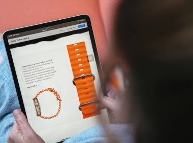 London, UK - 13 Eylül 2023: Watch Ultra Serisi 2 'yi Apple Computers web sitesinde satın almaya kendini kaptırmış bir kadın canlı turuncu okyanus bandının detaylarını araştırıyor.