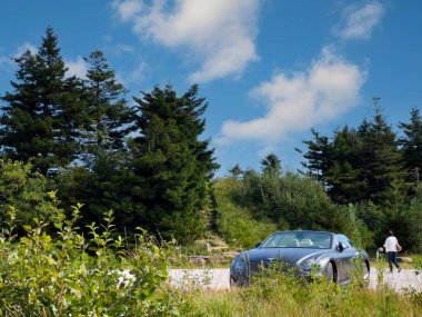 Mummelsee, Almanya - 17 Eylül 2023: Bir kadın, arka planda köknar ağaçları tarafından çerçevelenmiş, doğayla harmanlanmış, park halindeki üstü açık bir Bentley 'den uzaklaşırken görüldü.