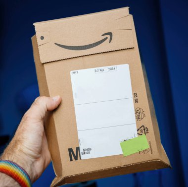Paris, Fransa - 5 Temmuz 2023: Erkek el mavi arkaplana karşı bir Amazon M paketi tutuyor, gelen paketleri ve markaların imza rengini vurguluyor