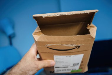 Paris, Fransa - 5 Temmuz 2023: Amazon Prime karton paketini mavi arka planda açık tutan bir erkeğin POV 'u, yeni bir teslimatın birinci şahıs görüntüsünü sunuyor