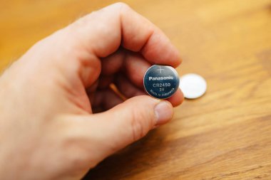 Hamburg, Almanya - 27 Mart 2023: Makro yakın plan çekimde, bir erkek eli Panasonic CR2032 3V lityum bataryasını tutuyor, üzerinde 