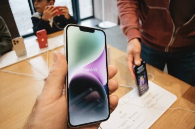 Paris, Fransa - 22 Eylül 2022: En son Apple iPhone 14 'ü elinde tutan bir erkek el görülürken, diğer müşteriler fırlatma günü arka planda çeşitli telefonları inceliyorlar..