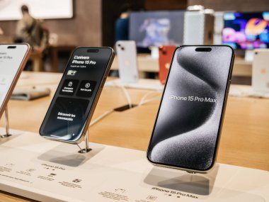 Paris, France - Sep 22, 2023: A row of the newly-released titanium iPhone 15 Pro smartphones by Apple Computers is displayed inside an Apple Store, with customers actively shopping in the background clipart