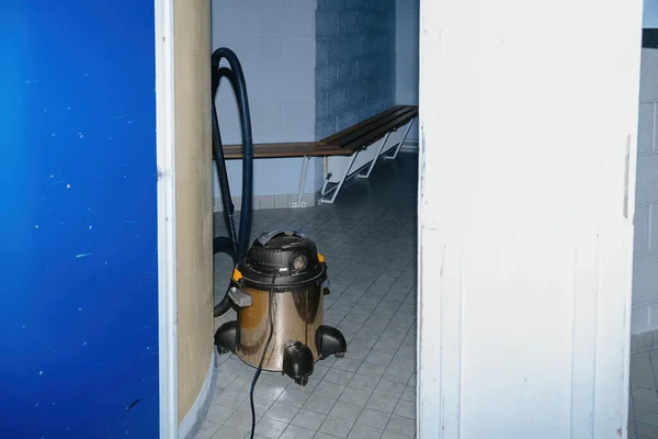 Industrial-grade vacuum cleaner left unattended in a large hallway within an educational facility.
