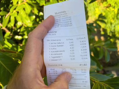 Almanya - 27 Şubat 2023: Etten suya çeşitli ürünleri listeleyen bir restoranın makbuzu bir erkeğin elinde toplam 41.8 avro.
