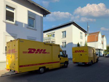 Kehl, Almanya - 29 Eylül 2023: Bir şehir merkezinde yan yana park edilmiş iki sarı DHL teslimat aracı, yakındaki apartmanlara yakın konumdalar..