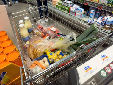 Almanya - Sep 29, 2023: Bir Alman süpermarketinde bulunan süt, mantar, domates, havuç ve diğer gıda maddeleriyle dolu bir süpermarket arabasının tepeden tırnağa görüntüsü
