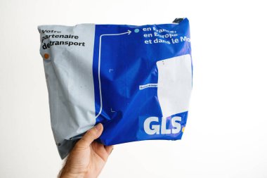 Paris, Fransa - Sep 6, 2023: Bir erkek eli GLS paketini titizlikle tutuyor, izole edilmiş beyaz bir arkaplana mükemmel çerçevelenmiş, güvenli ve verimli paket işleme odaklarını vurguluyor
