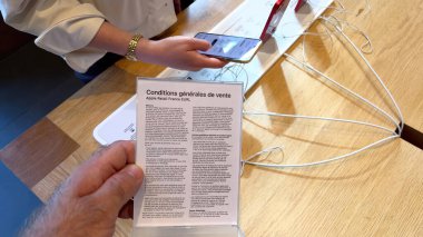 Paris, Fransa - 23 Eylül 2023: Bir erkek, Appre Perakende Fransa 'yı EURLs Genel Satış Koşullarını, arka planda bir kadın olarak bir iPhone 15 Pro için alışverişe daldı.