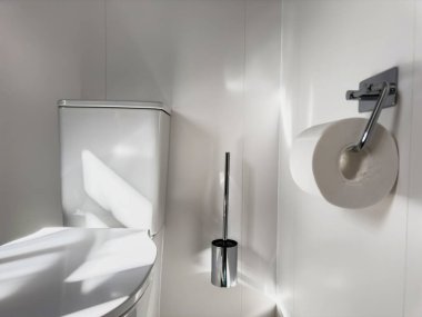 Cilalanmış krom tuvalet kağıdı tutacağı, fırçası ve porselen tuvaleti olan modern banyo.