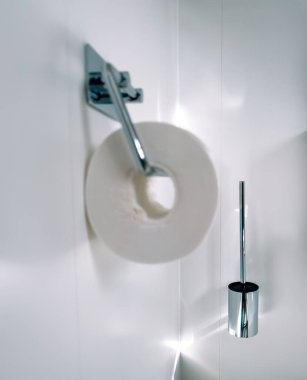 Modern bir banyoda, odak noktası krom tuvalet fırçasının yanındaki tuvalet kağıdı tutacağıdır.
