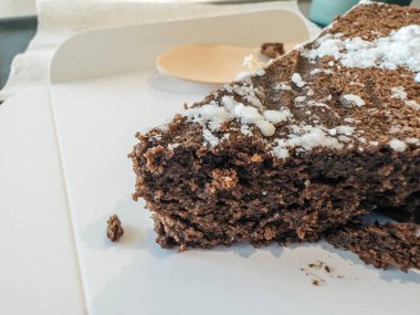 Kafe kâğıt tepside sunulan çikolatalı pasta, ahşap bir kaşık arka planında.