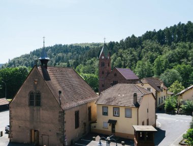 Yükselmiş bir perspektif Abbaye de Graufthal kilisesini ön planda belirgin bir şekilde yakalar, Eglise Protestanı Graufthal arka planda dimdik durur.