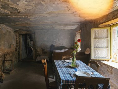 Geniş açılı bir bakış açısı, masa, sandalye ve yatak ile döşenmiş antik bir troglodit evin içini, açık bir pencere ve çiçekli bir vazoya sahip, tarihsel bir bakış sunan,