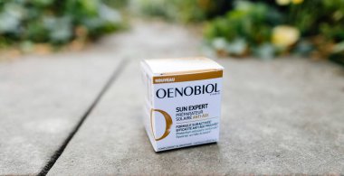 Paris, Fransa - 30 Mayıs 2023: Oenobiol Paris Sun Expert marka cilt bakımı kutusu, arka planda yeşil yaprakların bulanıklaştığı beton bir yola yerleştirilir.