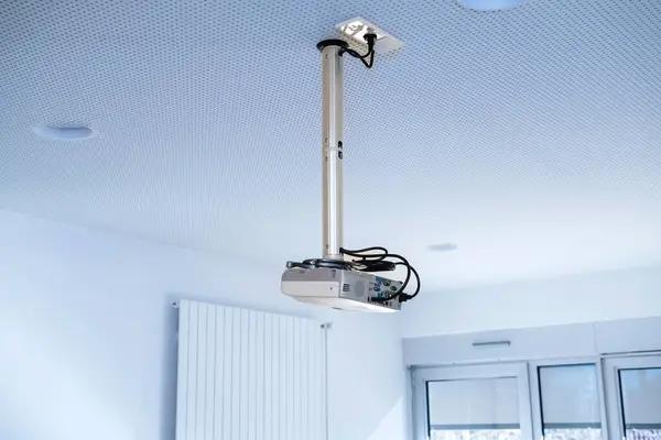 A blue-hued projector inside an office interior, mounted on a steel pole suspended from the ceiling