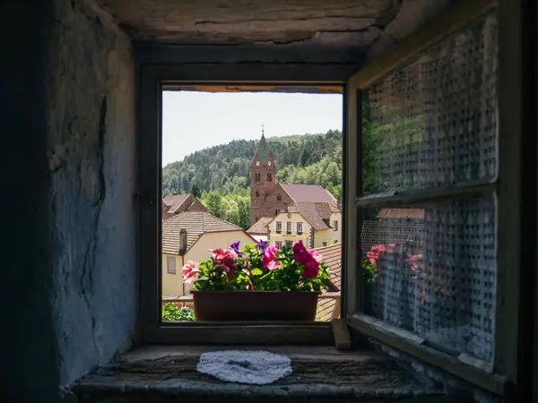 From a unique vantage point inside a troglodyte dwelling, an open window offers a captivating frame, highlighting the distant Eglise protestante Grauftha