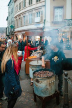 Colmar 'daki Noel pazarında lezzetli sıcak kavrulmuş kestane alışverişi yapan insanların dikkati dağılmış bir bakış açısı, festival sahnesine rüya gibi bir ortam ekliyor.