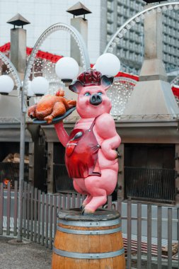 Pariss La Savunma Noel pazarındaki hareketli market tezgahlarının önünde elinde tavuk tutan bir domuzu resmeden eşsiz bir anıt.