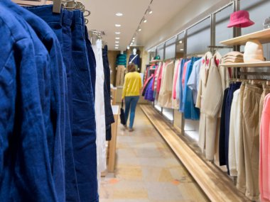 Moda koleksiyonuna yeni ürünler ve aksesuarlar ekleyen, bir giyim mağazasının içinden alışveriş yapan şık görünümlü, tanınmamış bir kadının silüeti.