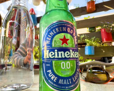 Kintzheim, Fransa - 4 Ekim 2023: Alkolsüz Heineken bira şişesi, her ikisi de açık teras masasındaki restoranlarda sergileniyor..
