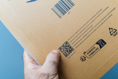 Paris, Fransa - 25 Ekim 2023: Bir sürücü, paket malzemelerinin geri dönüşümü hakkında ayrıntılı bilgi sağlayan bir QR kodu içeren Amazon Prime karton paketini elinde tutuyor