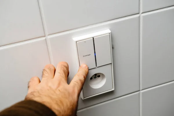 View from the perspective of a male hand operating a light switch and power outlet with German classical design, featuring the word eclairage translated as lighting
