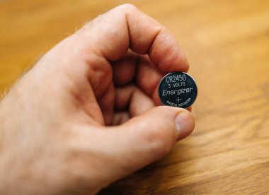 Hamburg, Almanya - 27 Mart 2023: Energizer CD 2425 madeni para bataryasını elinde tutan erkek el, Endonezya 'da gururla üretilmiş, cihazlar için güvenilir güç sağlıyor. Ahşap masa arkaplanı