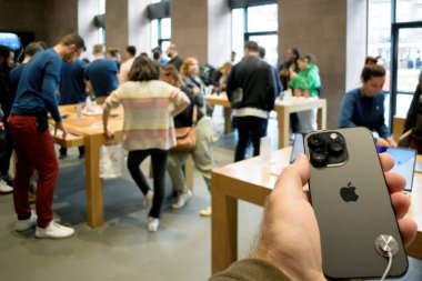 Paris, Fransa - 22 Eylül 2022: En son iPhone 15 Pro Max 'i müşterilerle dolu bir Apple mağazasının bulanık arka planına sahip bir erkeğin yakın çekimi