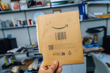 Erkek el, Amazon Prime karton paketini tutuyor, gülümseyen ok logosunu ve geri dönüşüm talimatlarını gösteriyor, sorumlu ambalajı sembolize ediyor.