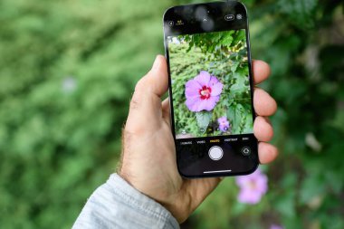 Londra, Birleşik Krallık - 28 Eylül 2022: Bir bakış açısı, yeni Apple Computers iPhone 14 Pro 'yu elinde tutan bir erkeği ön planda bir amber çiçeği ve çözünmüş bir bokeh ile yakalıyor.