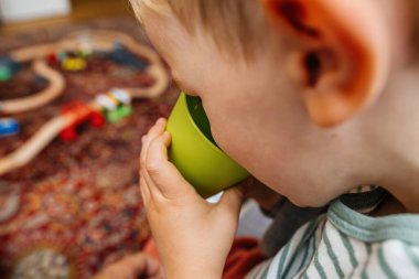 Yeni yürümeye başlayan çocuk yeni plastik yeşil bardağından taze, temiz su içiyor, sağlıklı alışkanlıkları simgeliyor.
