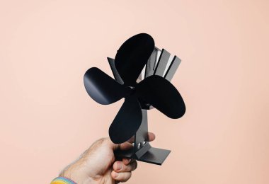 Siyah, güçsüz bir soba vantilatörü tutan erkek el daha iyi ısı dağılımı ve yakıt tüketimini yüzde 15 azaltmak için kullanışlı.