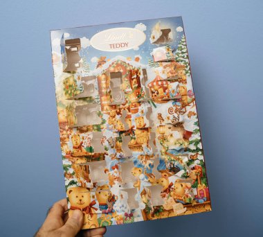 Paris, France - Dec 20, 2023: Against a blue background, a male hand holds an empty Lindt teddy advent calendar, showcasing that no chocolates remain inside