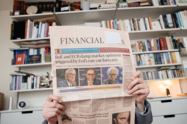 Paris, France - Dec 20, 2023: A woman in a living room reads the latest Financial Times, featuring headlines about the BoE and ECBs impact on market optimism after the Feds rate cut