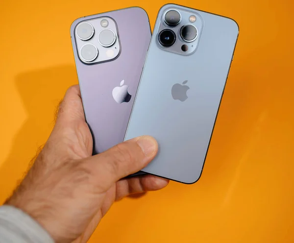 2022年10月27日 法国巴黎 展示了一只手扶着紫色和蓝色Iphone并排的人 其橙色背景鲜明地凸显了智能手机的流畅设计 — 图库照片