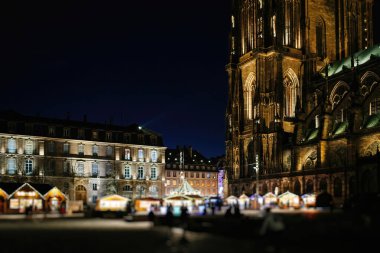 Strasbourg 'da Gotik bir katedralin yanında, yıldızlı gece gökyüzünün altında parlak bir şekilde aydınlatılmış canlı bir açık hava pazarı.