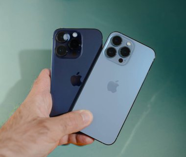 Paris, Fransa - Sep 29, 2023: Bir müşteri gururla en son Apple Computers iPhone 15 Pro ve 14 Pro akıllı telefonlarını canlı bir Cyan arka planına karşı sergiliyor ve çarpıcı bir karşıtlık yaratıyor