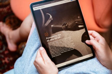 Londra, İngiltere - 13 Eylül 2023: Bir kişi rahatça oturmuş, bir tablet ekrandan okumaya dalmış, bu ekranda Apple Watch Ultra ile ilgili bir reklam veya makale gibi görünüyor.