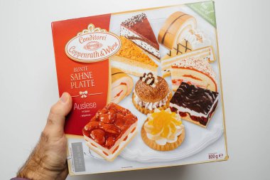 Frankfurt, Almanya - 31 Ekim 2023: Bir el beyaz bir arkaplana karşı bir kutu Conditorei Coppenrath Wiese Bunte Sahne Platte çeşitli pastalar tutuyor.