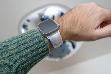 Bremen, Almanya - 28 Aralık 2023: Elma Saati Ultra 2 akıllı kol bandı tutan bir erkek gökkuşağı bayrağı ve metin içeren bir bileklikle süslenmiştir.