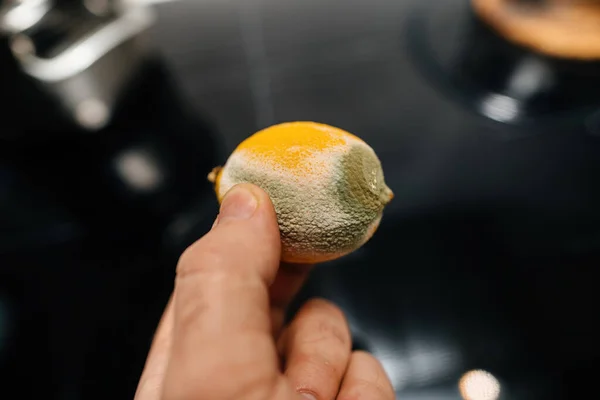 A male hand holds a yellow lemon on a sleek black glass kitchen background, creating a striking contrast and adding a touch of freshness to the modern kitchen setting