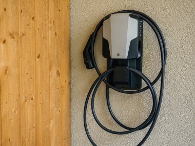 Ahşap bir cephenin yanında duvara monte edilmiş elektrikli araç şarjı, yerleşim alanlarında temiz enerjinin entegrasyonunu vurguluyor..