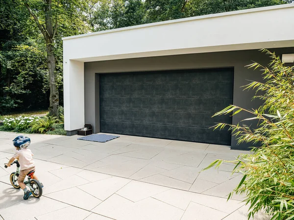 Genç bir çocuk, modern mimarinin yanındaki banliyö yolunda bisiklet sürüyor..