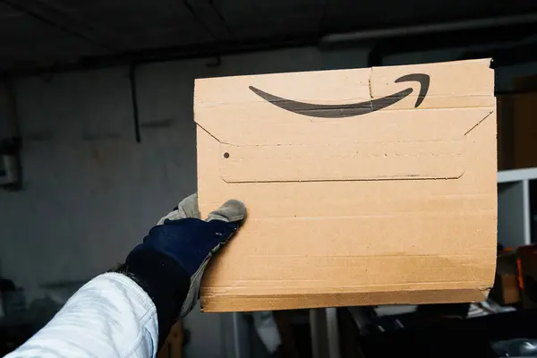2023年12月10日 ドイツのブレーメン 大きな倉庫にアマゾンプライムのボール紙小包を提示する男性手 オンラインショッピングと迅速な配送サービスの効率性と利便性を紹介 — ストック写真